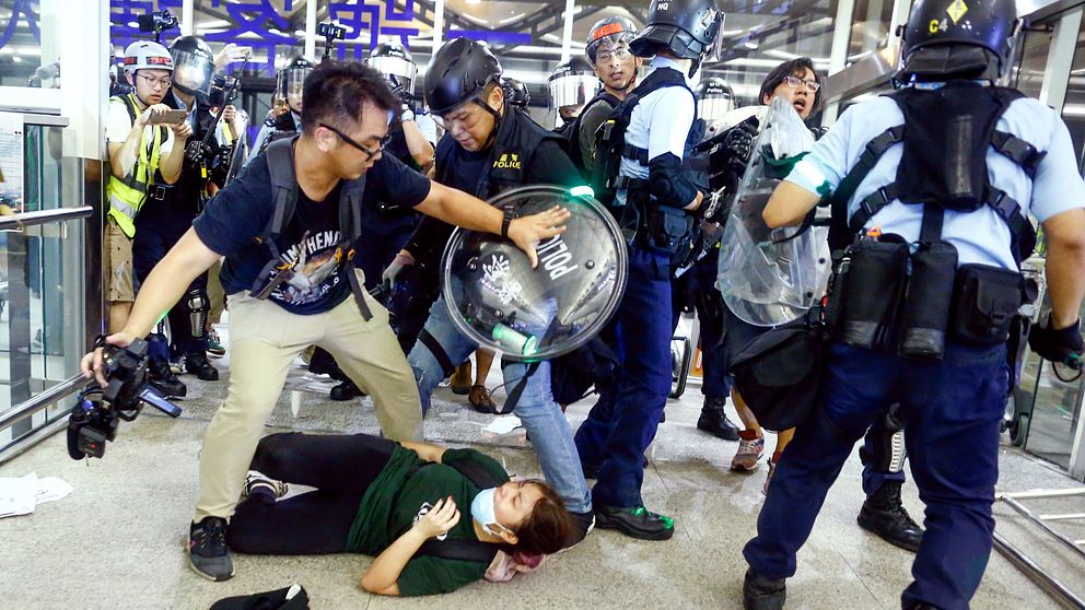 Kvinnlig demonstrant ligger på golvet medan polis och demonstranter bråkar.