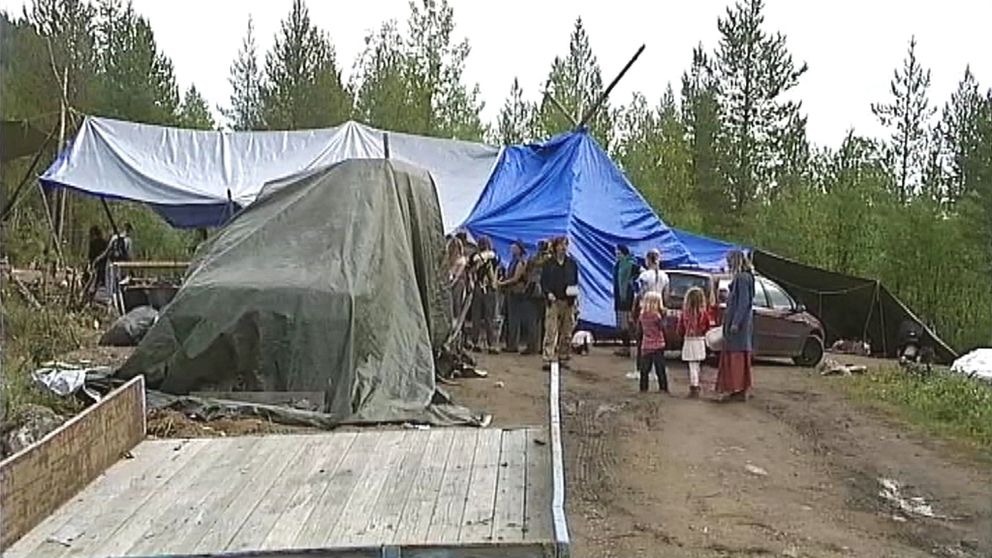 några personer på öppen plats i skogen, presenningar uppspända som tält-tak.