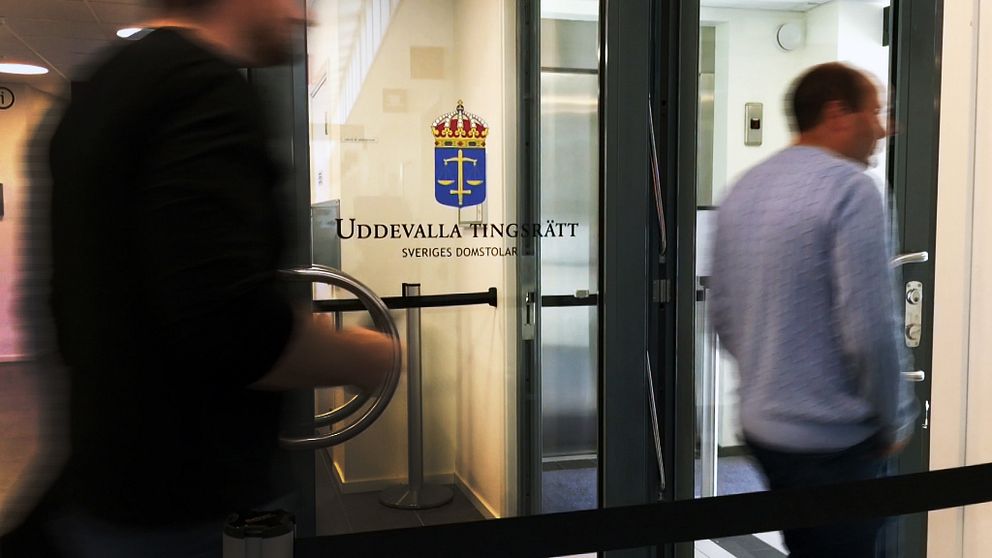 Två personer passerar förbi dörr med text ”uddevalla tingsrätt”