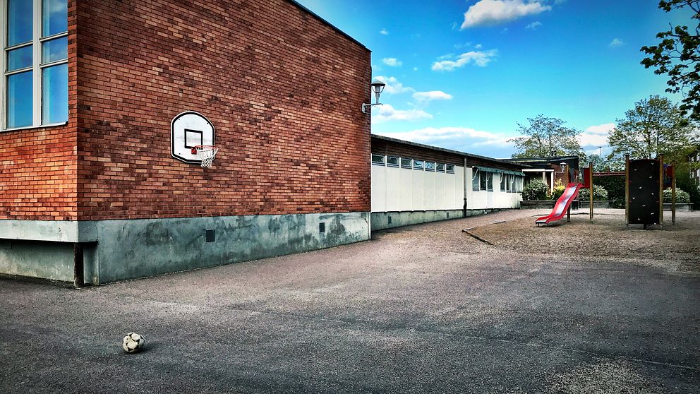 Skolbyggnad och asfalterad skolgård med lekplats