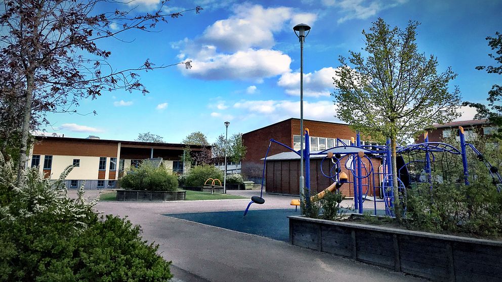 Skolbyggnader och asfalterad skolgård med lekplats