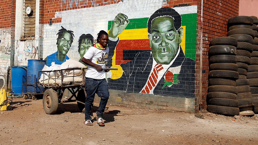 En ung man framför en muralmålning av Robert Mugabe i huvudstaden Harare
