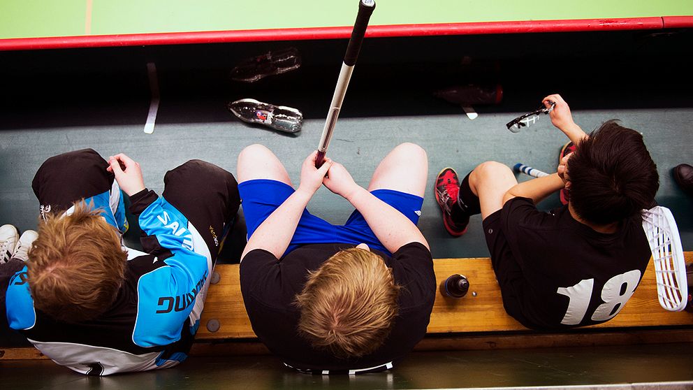 Tre barn som spelar innebandy sitter på avbytarbänken.