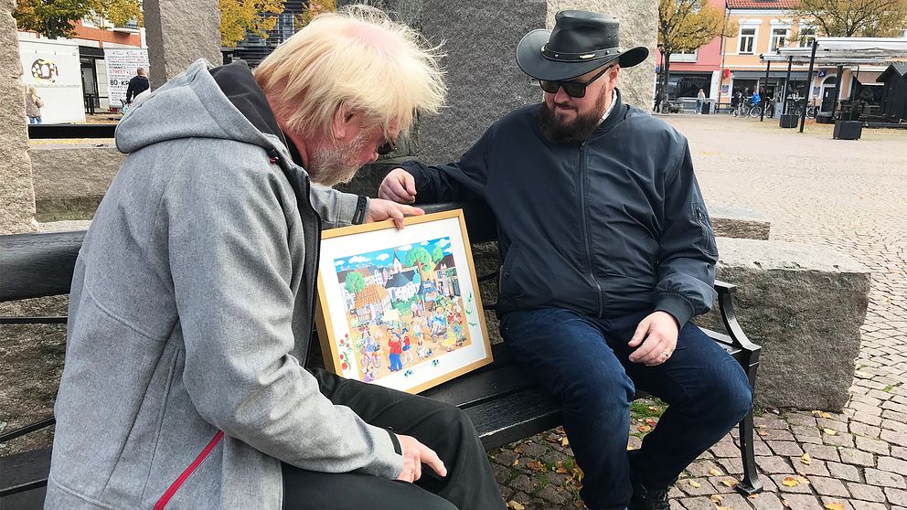 Initiativtagaren Fredrik Jansson och tidigare ordföranden Ewe Windahl tittar på ett konstverk av Rosfestivalen, målat av en lokal konstnär.