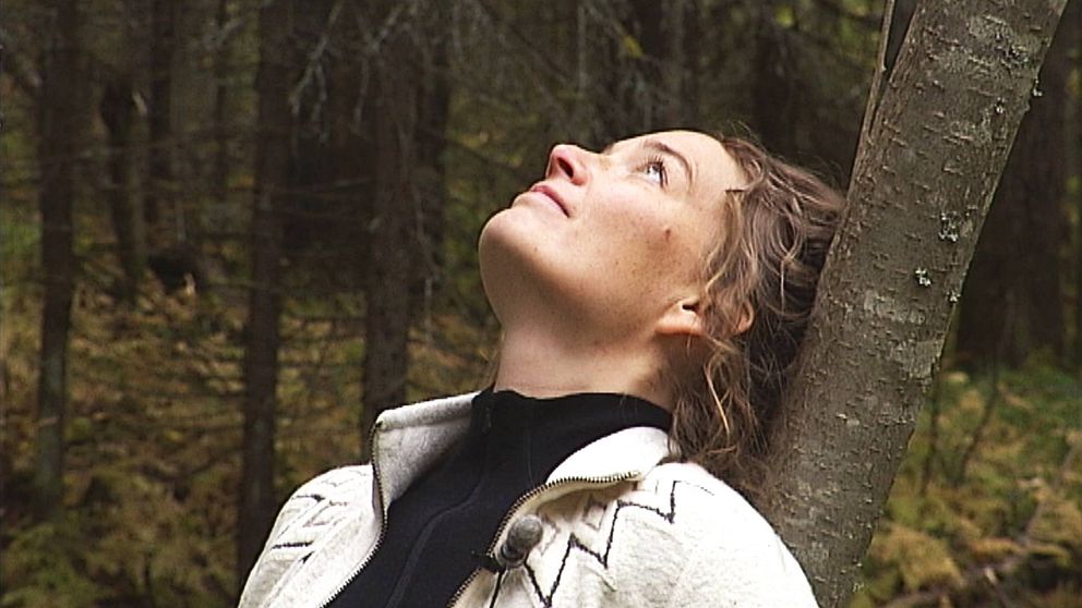 en kvinna som lutar sig bakåtmot ett träd i skogen och tittar uppåt