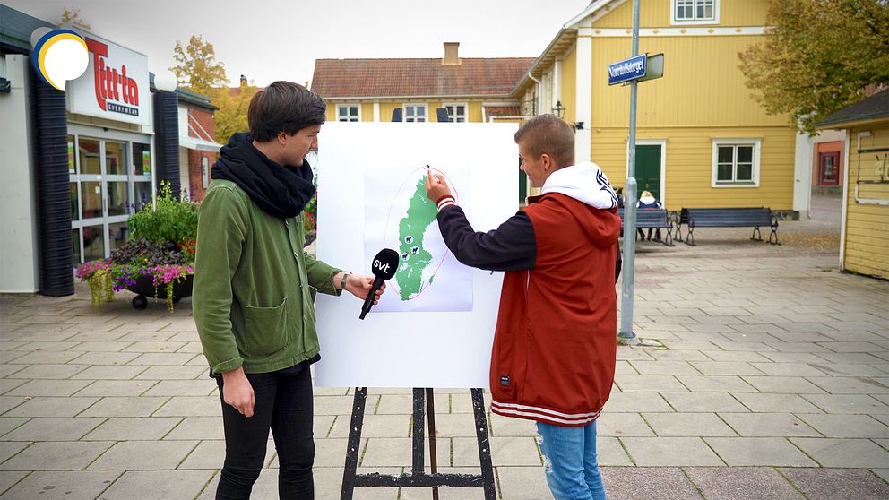 Reporter Torbjörn Averås Skorup står på torget i Lindesberg med ett trebensstaffli. På stafflit står en bild med en Sverigekarta.