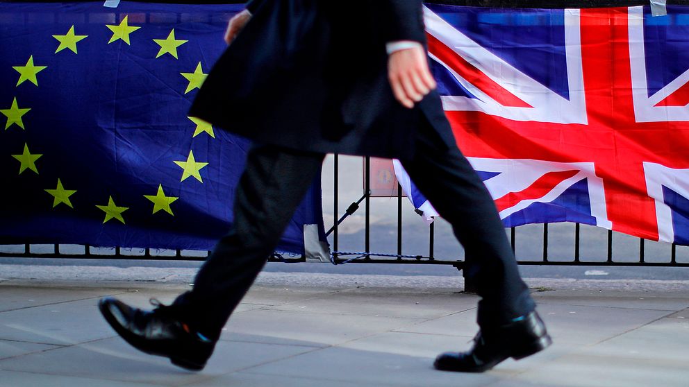 Bild på person som passerar den brittiska flaggan och EU-flaggan som kan symbolisera att Storbritannien snart kommer att lämna den Europeiska unionen (EU).