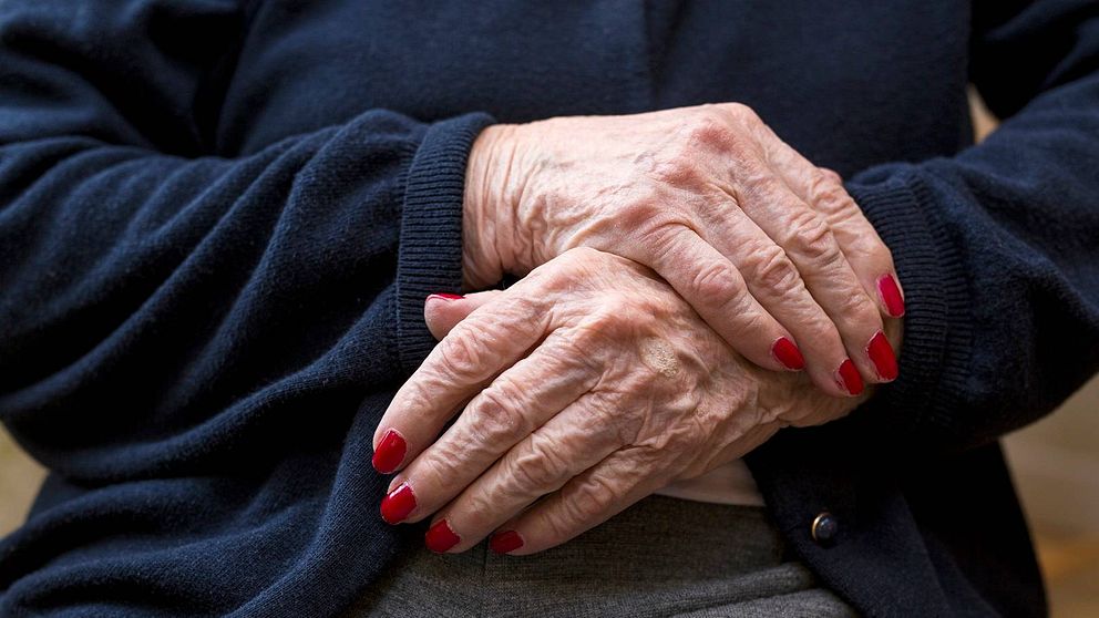 bild på äldre persons händer, med naglar målade med rött nagellack