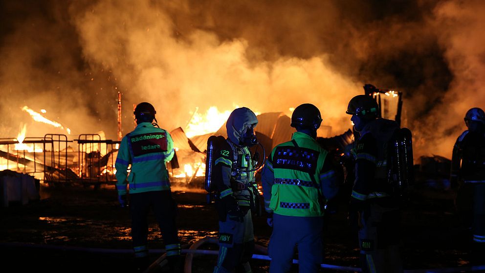 räddningspersonal framför resterna av en brinnande byggnad