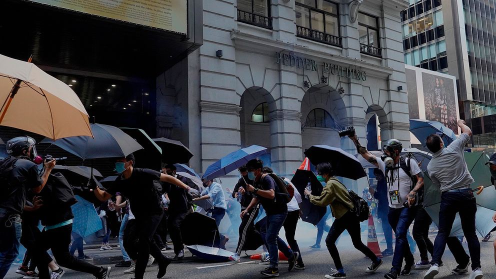 Protestanter med paraplyn beskjuts av polisen med tårgas under måndagen i Hongkong.