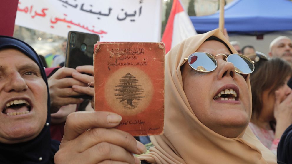 Kvinna håller upp en gammal libanesisk id-handling mitt under protesterna.