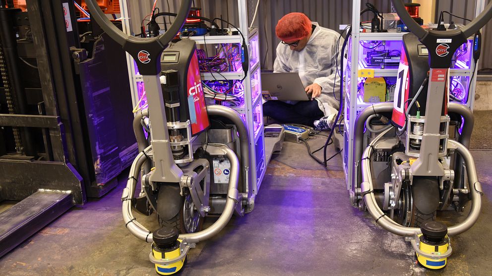 Forskare sitter på golvet och programerar lagerrobotar.