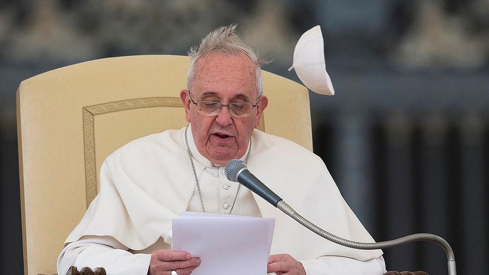 A gust of wind blows away Pope Francis' cap as he delivers his message during his weekly general audience in St. Peter's Square at the Vatican, Wednesday, Feb. 19, 2014