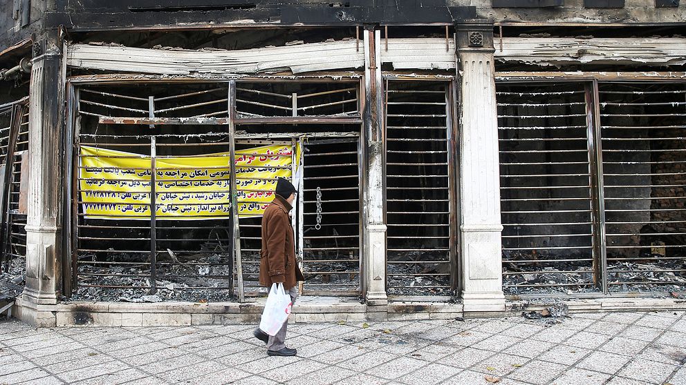 En man passerar en utbränd bank som stacks i brand under iranska protester mot höjda bränslepriser.