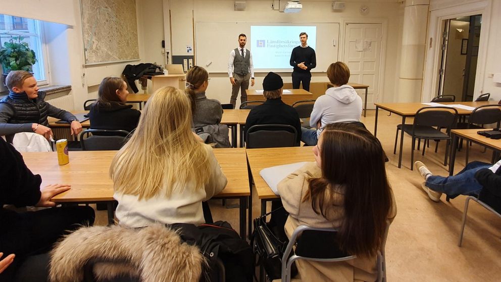 Elever lyssnar på två män som föreläser i ett klassrum.