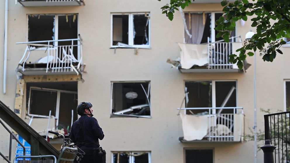 Skadade balkonger på en husfasad efter explosionen i Linköping. En polis med hjälm tittar upp mot fasaden.
