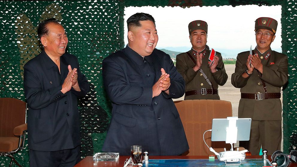 Nordkoreas ledare Kim Jong-Un omgiven av applåderande militärer vid ett skrivbord.