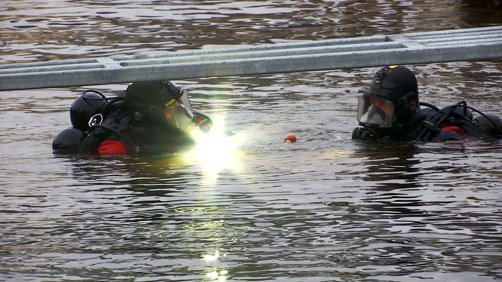 Två män i vattnet i dykutrustning men ficklampa som lyser in i kameran