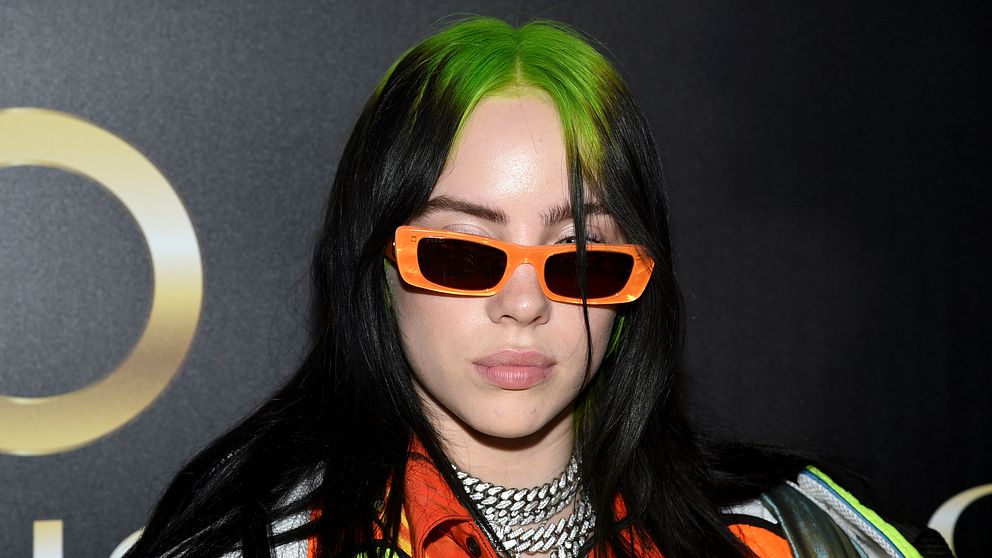 Billie Eilish på röda mattan. Hon har orangea solglasögon på sig.