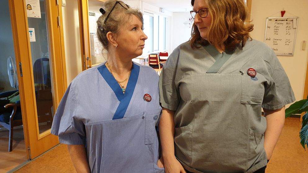 Två undersköterskor står i korridoren och tittar på varandra.