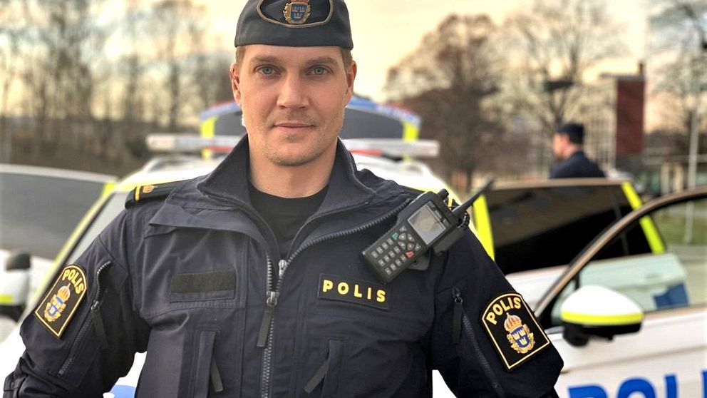 Uniformerad polis står uppställd framför en polisbil.