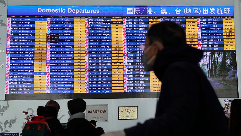 En passagerar med skyddsmask på flygplatsen i Peking tittar på avgångstavlan i terminalen. Sedan virusets utbrott har Kina begränsat möjligheterna att resa i landet