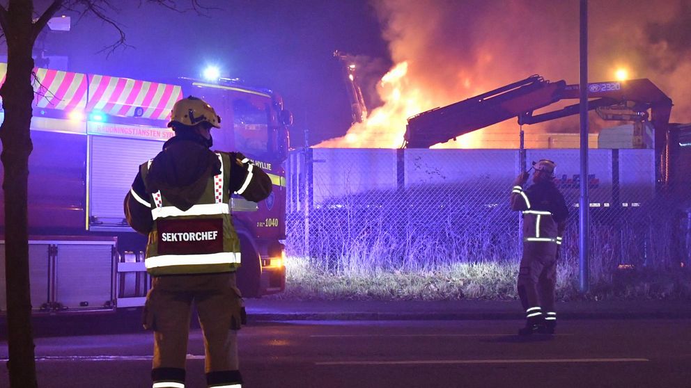 Två personer från Räddningstjänsten framför brinnande lastbilar