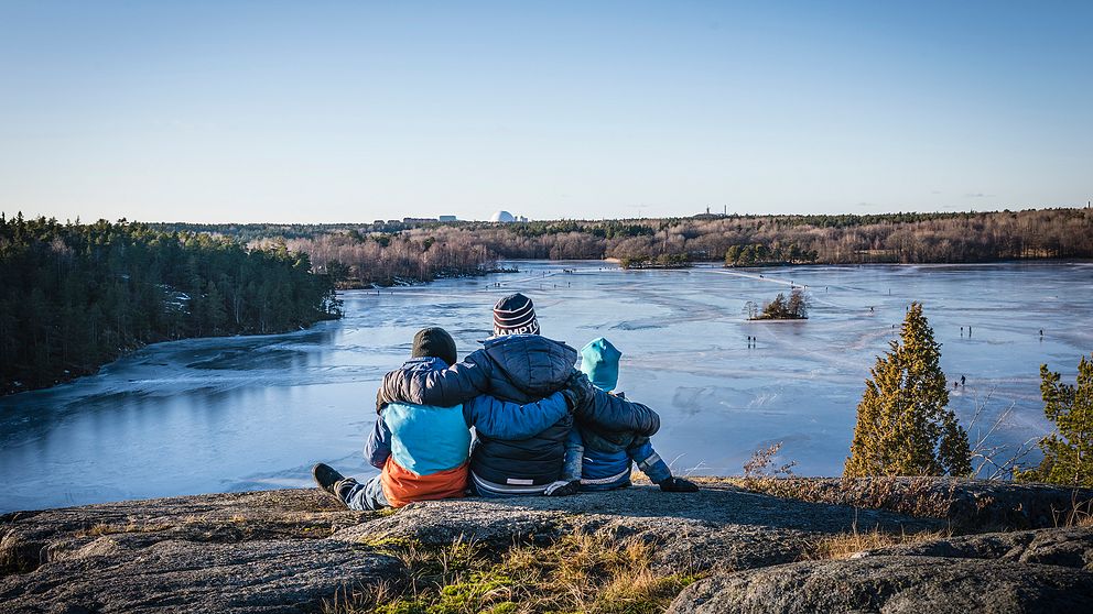 Tre personer sitter på klippa med utsikt över sjö.