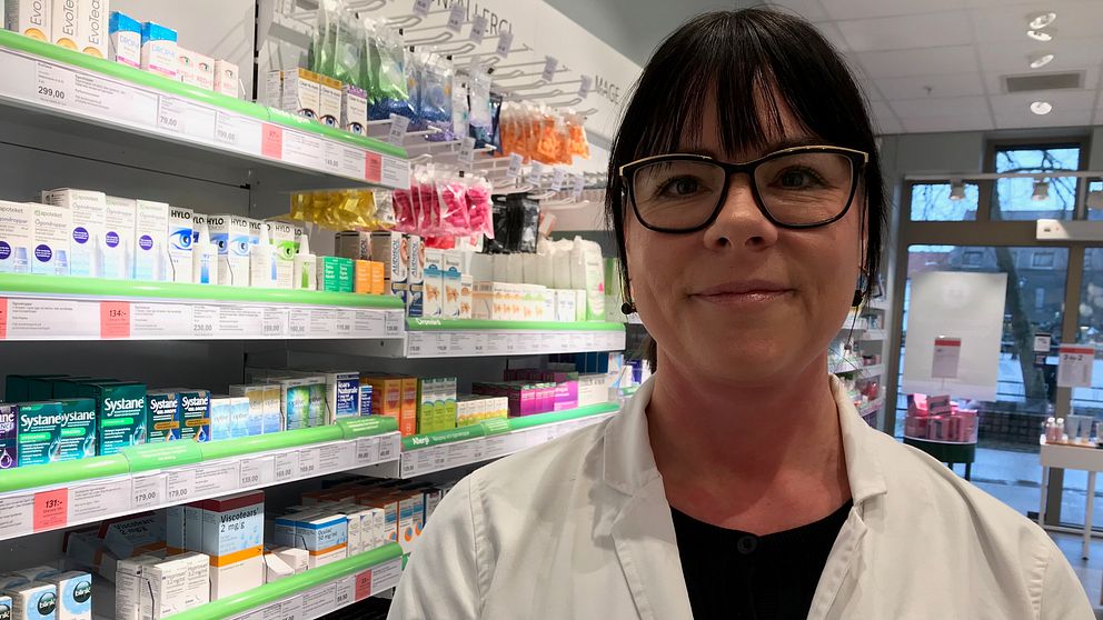 Säljledaren Helena står vid en hylla på ett apotek fyllt med allergimedicin. Hon har glasögon på sig och en vit rock.