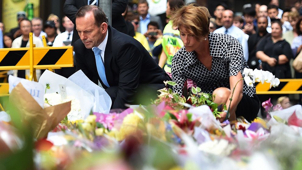 Premiärminister Tony Abbott (L) och hans fru Margaret lägger ner blommor nära den plats där det blodiga gisslandramat fick sitt slut.