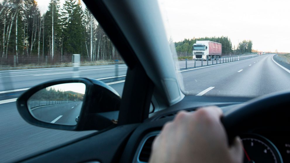 Händer på ratt som kör bil på motorväg.