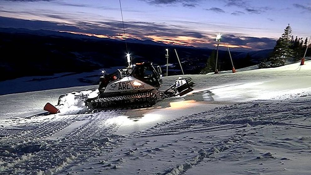 Pistmaskin preparerar skidbacke i Åre under skymningen med berg i bakgrunden.