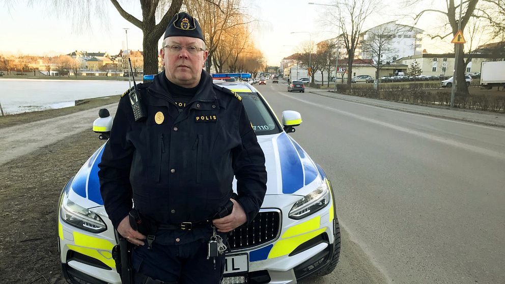 Porträttbild på polisen Erling Arvidsson som står framför en polisbil utmed en bilväg.