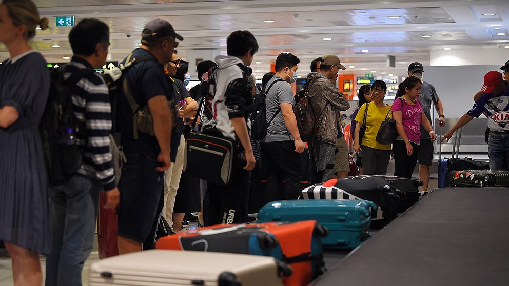 Personer står och väntar på bagage på flygplats.