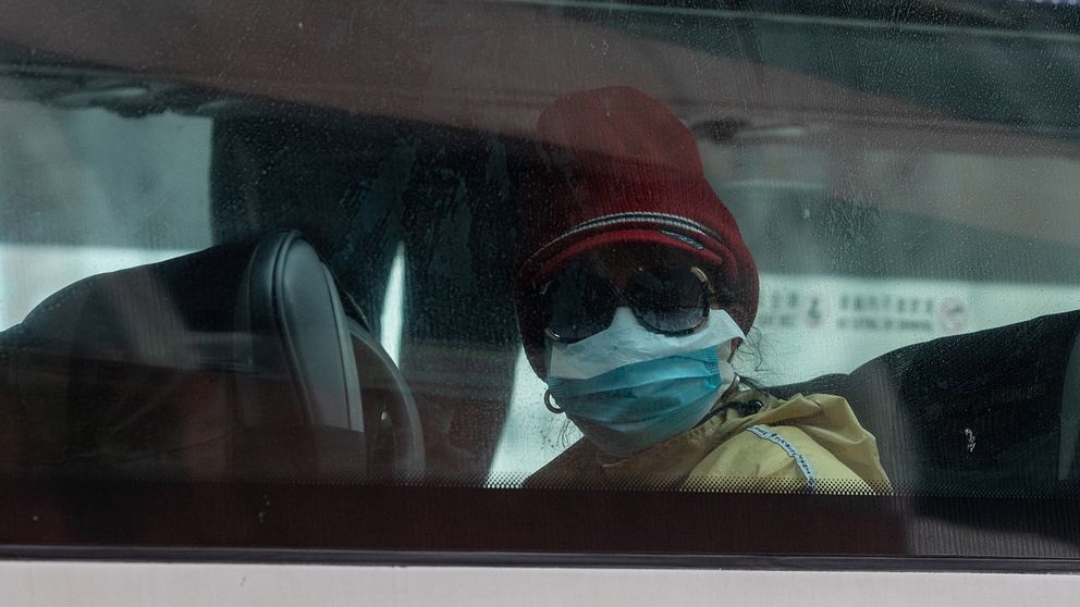Kvinna med ansiktsmask och solglasögon sitter på en buss.