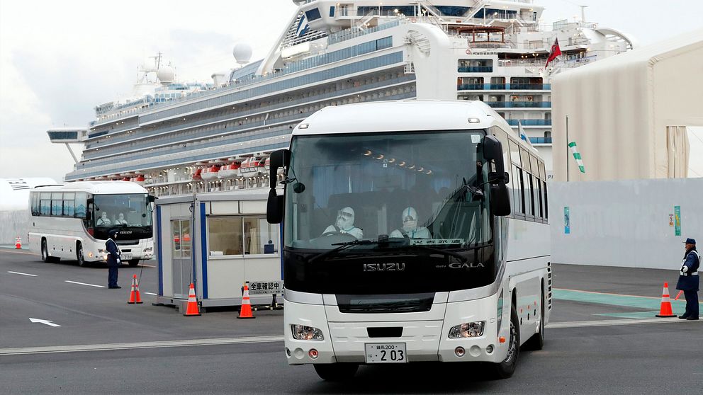 En buss med passagerare som varit ombord på Diamond Princess får lämna hamnen i Yokohama i Japan. I bakgrunden syns fartyget.