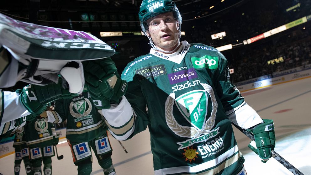 Marcus Nilsson i en grönvit Färjestadströja med lagkamrater i bakgrunden inne i Löfbergs arena.