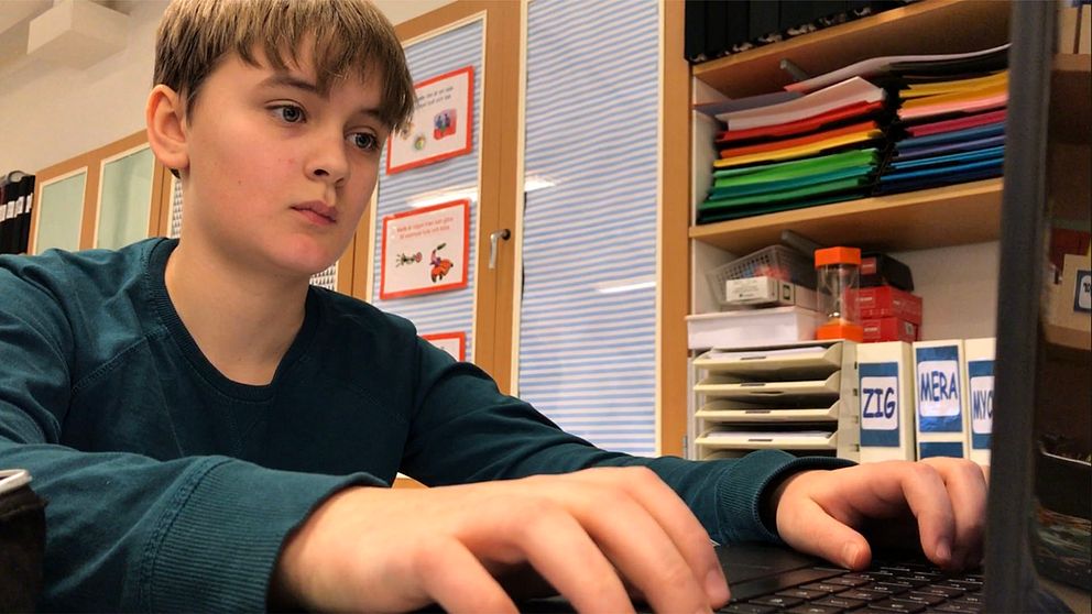 En bild på en pojke i femte klass som skriver på en dator. Han sitter i ett klassrum.