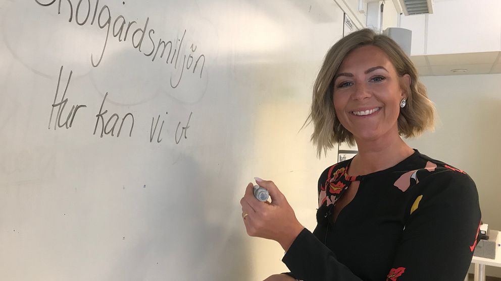 Kvinna skriver på whiteboard-tavla i klassrum.