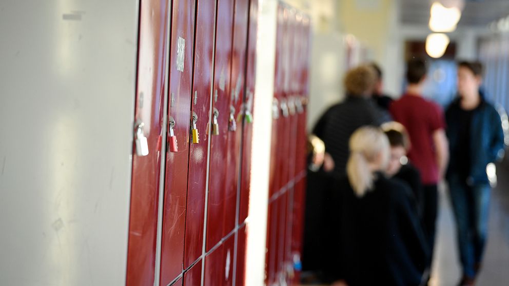 Skolelever som sitter i en skolkorridor med låsta skåp.