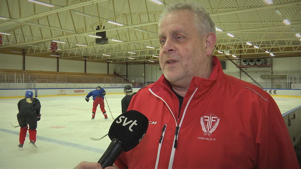 Christer Larsson i röd jacka blir intervjuad vid sidan av hockeyrinken. Tre spelare syns i bakgrunden.