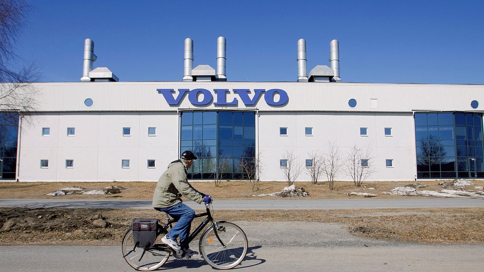 En stor fabriksfasad med en Volvoskylt på. I förgrunden cyklar en man förbi och tittar mot byggnaden.