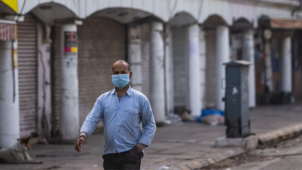 Man med munskydd går på en folktom gata i New Delhi.
