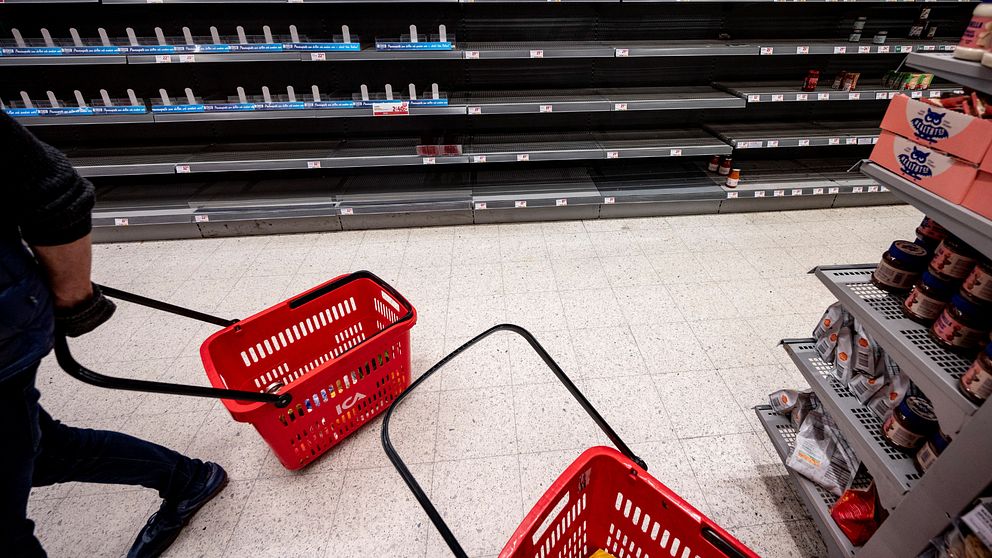 En tom butikshylla i bakgrunden, framför en kundkorg som dras av en man.