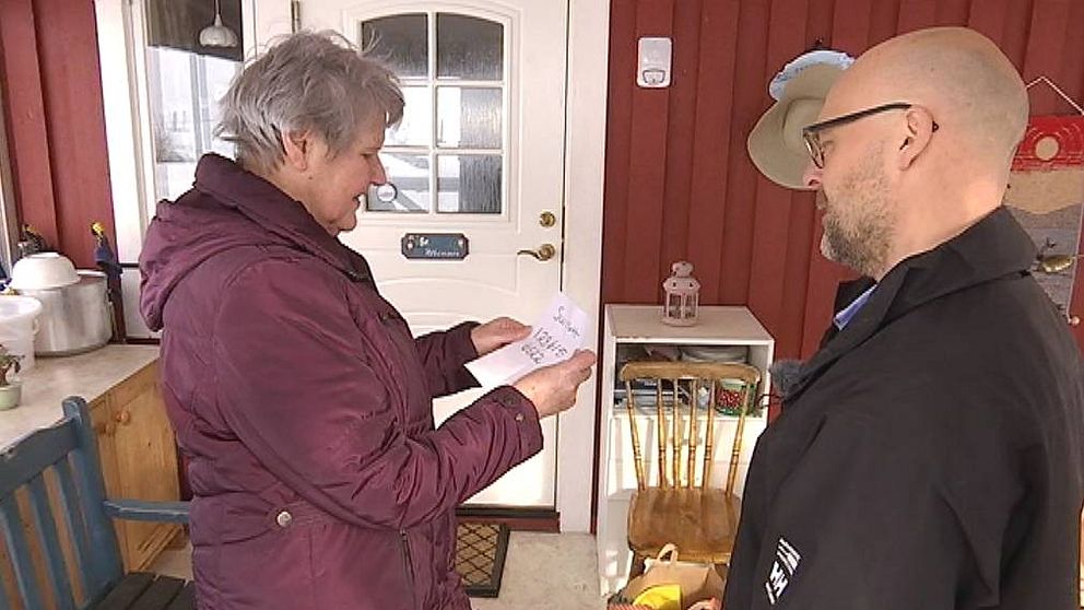 Äldre gråhårig kvinna tar emot matkassar av en yngre skäggig man med glasögon