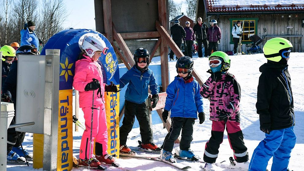 Skidåkande barn i färgglada kläder i liftkö i Tänndalen