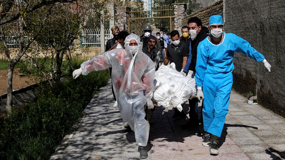 Människor i skyddsdräkter som bär en person som dött av covid-19 till en begravningsplats utanför Tehran.