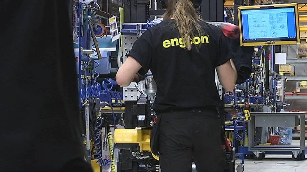 Tjej med svart t-shirt med texten Engcon i gult på ryggen, står vid en tiltrotator och monterar.