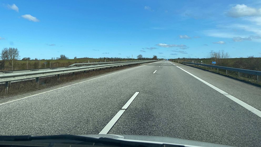 Bild tagen innifrån en bil, man ser en tom väg och blå himmel.