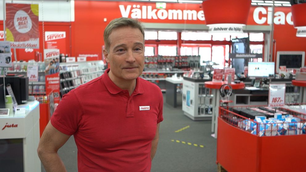 En man i röd tröja intervjuas i elektronikbutik